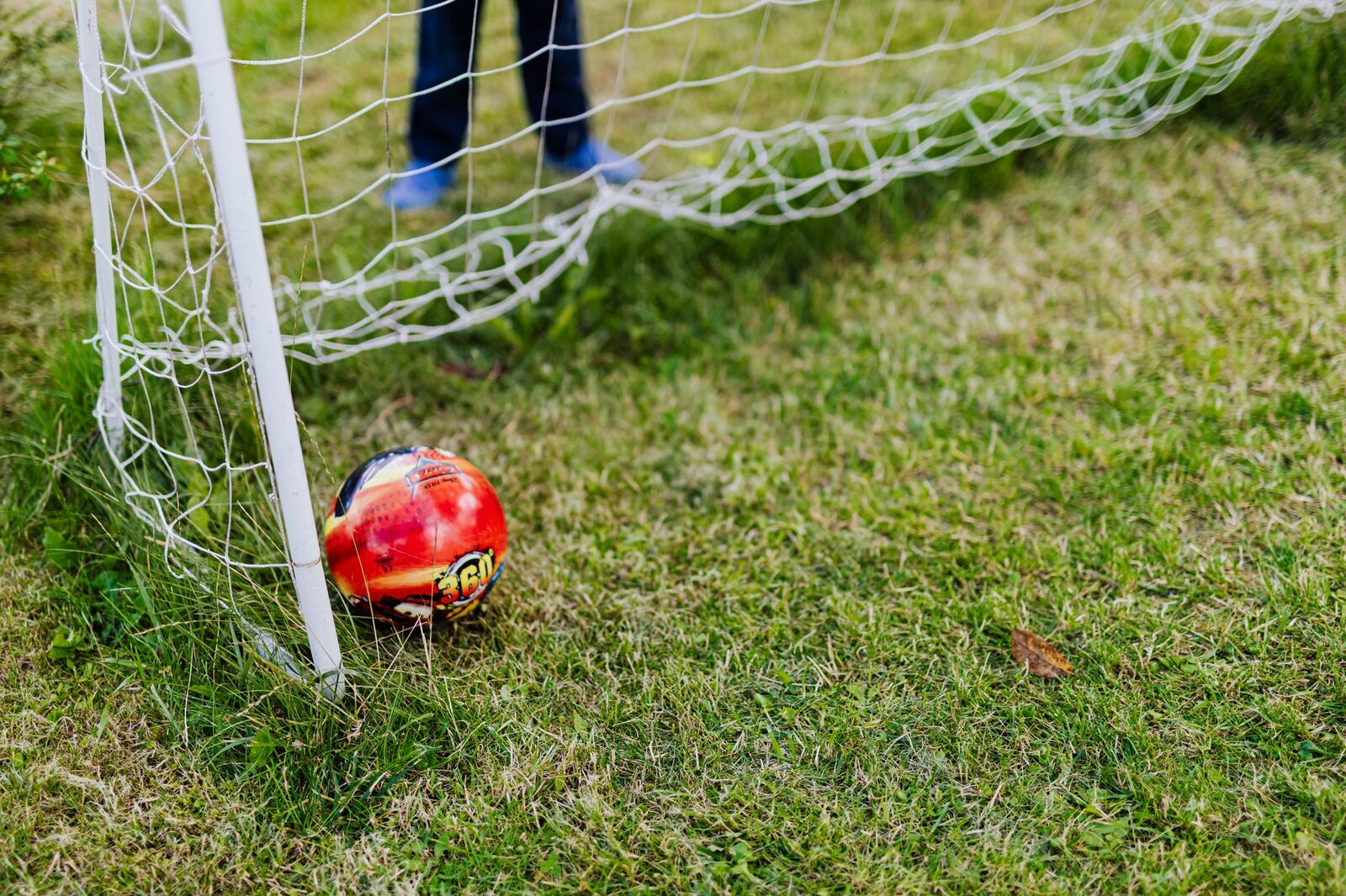 A football resting in the back of the net on a green pitch